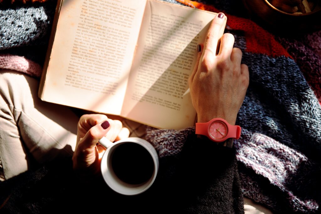 pessoa lendo um livro e tomando café